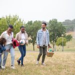 A joyful family walking through a park on a sunny day, carrying a picnic basket and a ball.